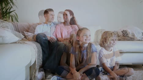 Siblings-sitting-on-the-floor-while-watching-tv-with-their-parents-behind-them