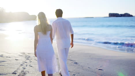 Couple-on-the-beach-walking-towards-the-sunset-while-holding-hands