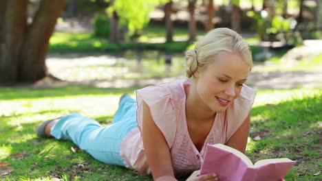 A-woman-lies-down-in-the-park-reading-as-she-then-looks-at-the-camera