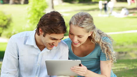 A-smiling-couple-use-a-tablet-pc-in-the-park-as-they-look-at-the-camera-at-the-end