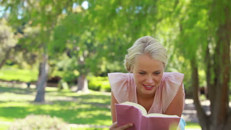 A-woman-lies-on-the-ground-and-reads-her-book-as-she-then-looks-at-the-camera