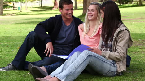 Three-friends-laughing-as-they-read-a-book-together-in-a-park