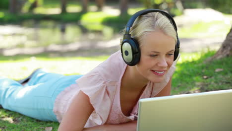 A-woman-lies-in-the-park-with-headphones-on-while-watching-a-laptop