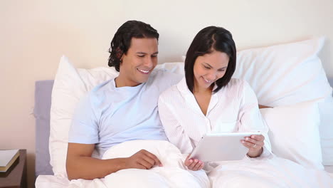Couple-sitting-on-their-bed-with-tablet-computer