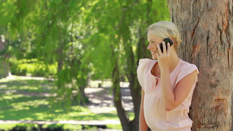 Una-Mujer-Parada-Junto-A-Un-árbol-Hablando-Por-Su-Teléfono-Mientras-Cuelga-Y-Mira-A-La-Cámara