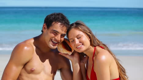 Smiling-couple-listening-to-a-seashell