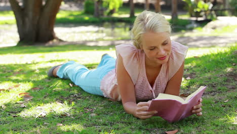 A-woman-lying-down-reading-a-book-in-the-park-as-she-then-looks-at-the-camera