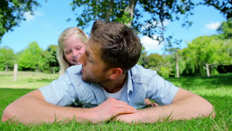 Father-smiling-while-lying-on-the-grass-before-his-daughter-peeks-her-head-out-from-behind-him