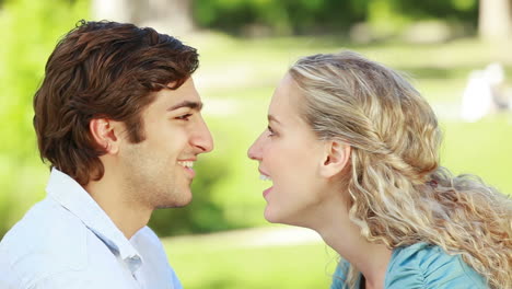 A-couple-look-at-each-other-as-they-kiss-in-the-park-and-then-look-at-the-camera