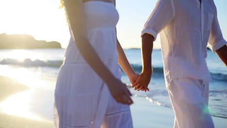 Couple-holding-hands-while-they-walk-along-the-beach