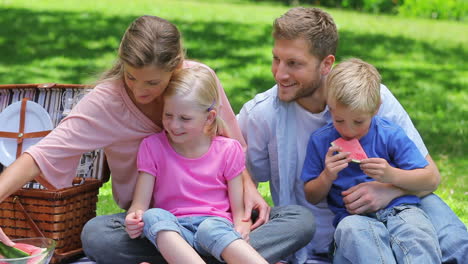 A-mother-handing-a-slice-of-watermelon-each-to-her-children-and-a-sandwich-to-her-husband