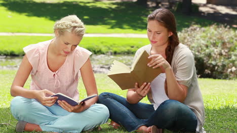 Two-women-read-books-in-the-park-as-one-shows-her-friend-her-book-and-they-laugh