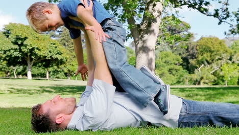 Un-Padre-Levanta-A-Su-Hijo-Por-Encima-De-él-Mientras-Yace-En-La-Hierba-Antes-De-Devolverlo-Al-Suelo