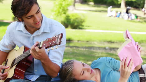 Man-practises-guitar-as-the-woman-rests-on-his-leg-and-reads