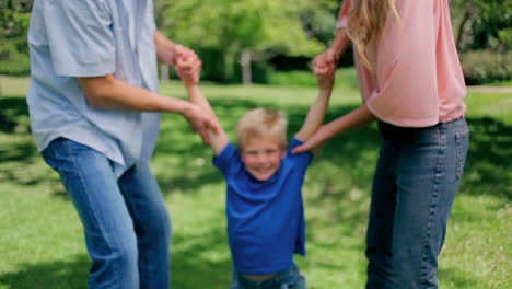 Niño-Siendo-Balanceado-Hacia-Adelante-Y-Hacia-Atrás-Por-Sus-Padres-Que-Sostienen-Sus-Brazos