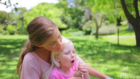A-woman-sits-with-her-daughter-who-is-blowing-a-dandelion-repeatedly-before-smiling