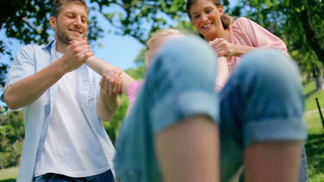 Two-parents-smile-as-they-swing-their-daughter-back-and-forth-by-his-arms-playfully