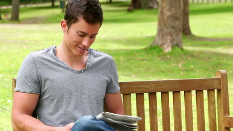 Man-reading-a-newspaper-before-looking-at-the-camera-as-he-sits-on-a-bench