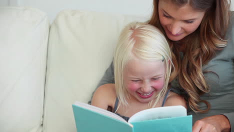 Girl-laughing-as-she-reads-a-book-with-her-mother