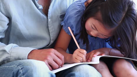 Una-Niña-Coloreando-Un-Libro-En-El-Regazo-De-Su-Padre.