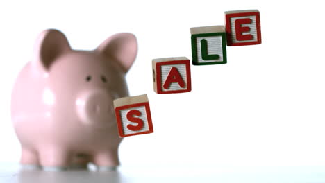 Alphabet-blocks-spelling-sale-falling-over-in-front-of-a-piggy-bank-