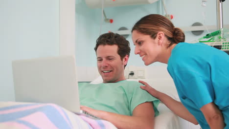 Happy-male-patient-typing-on-a-laptop-while-lying-on-a-bed