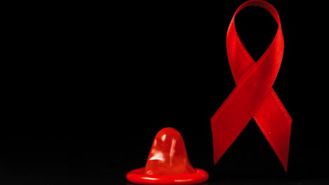 Condom-falling-over-in-front-of-a-red-ribbon-on-black-background