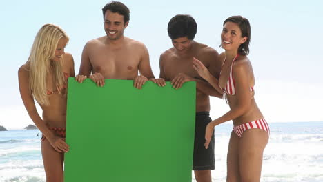 Amigos-Sosteniendo-Un-Tablero-Verde-En-La-Playa