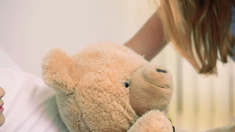 Smiling-woman-giving-a-teddy-bear-to-a-smiling-girl-in-a-bed