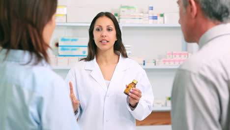 Female-pharmacist-talking-about-a-bottle-of-pills-behind-a-counter