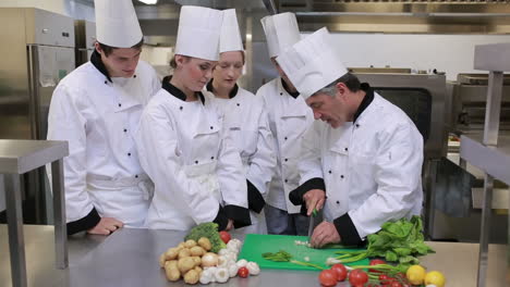 Cooks-watching-head-chef-slicing-vegetables