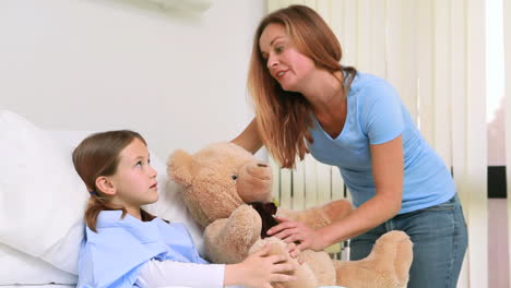 Smiling-woman-while-giving-a-teddy-bear-to-a-girl-in-a-bed