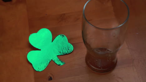 Hand-putting-down-empty-pint-beside-large-shamrock