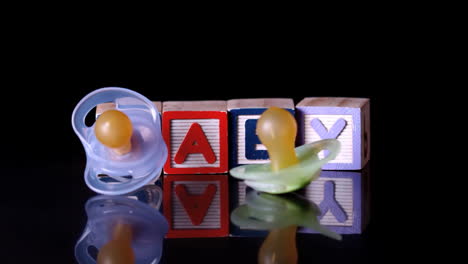 Pacifiers-falling-in-front-of-blocks-spelling-baby