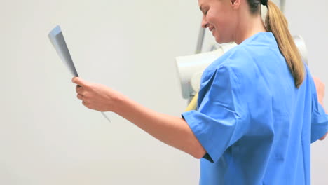 Smiling-nurse-holding-xray-while-proceeding-a-radiography-on-a-patient