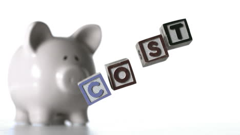 Blocks-spelling-cost-dropping-down-beside-a-piggy-bank