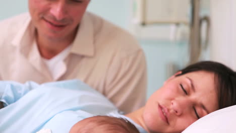 Padre-Feliz-Mirando-A-Su-Esposa-Y-A-Un-Bebé-Recién-Nacido-Durmiendo