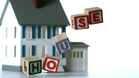 Blocks-spelling-house-falling-over-in-front-of-a-miniature-house-