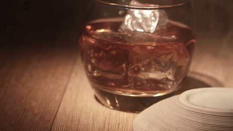 Cigar-being-placed-beside-tumbler-of-whiskey-on-the-rocks