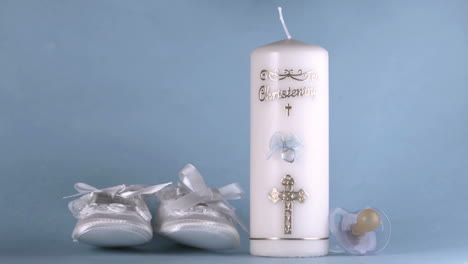 Baby-shoes-falling-beside-baptism-candle-on-blue-background