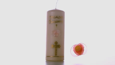Pink-pacifier-falling-beside-baptism-candle