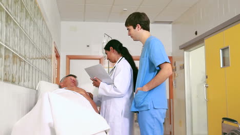 Médico-Y-Enfermera-Hablando-Con-Un-Paciente-Acostado-En-Una-Cama