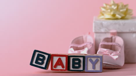 Baby-blocks-toppling-over-with-booties-and-gift-box-in-background