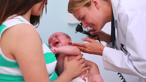 Doctor-examining-a-baby-with-an-otoscope-in-the-arms-of-his-mother