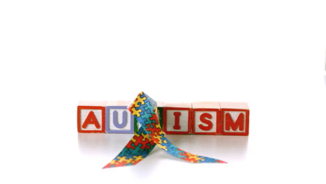 Awareness-ribbon-falling-onto-blocks-spelling-autism-on-white-background