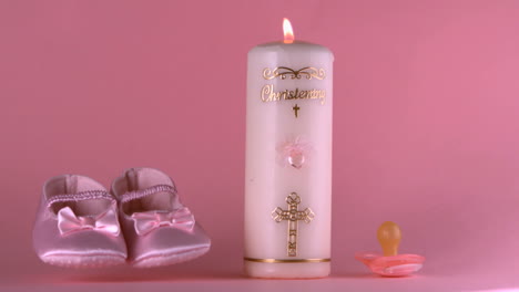 Baby-shoes-falling-beside-lit-baptism-candle-and-pacifier