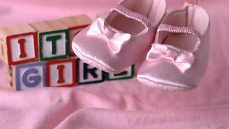 Babyschuhe-Fallen-Auf-Rosa-Decke-Mit-Der-Botschaft-„Es-Ist-Ein-Mädchen“-In-Blöcken