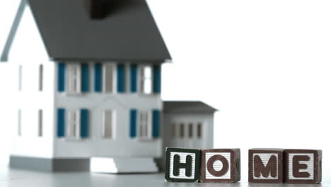 Blocks-spelling-home-sliding-along-in-front-of-a-miniature-house