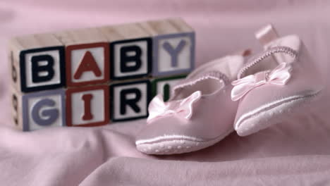 Baby-booties-falling-on-pink-blanket-with-baby-girl-message-in-blocks