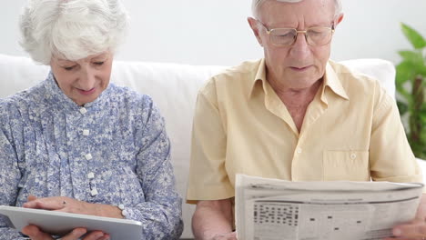 Old-couple-using-a-newspaper-and-a-tablet-